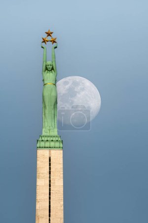 RIGA, Letonia - 0CTOBER 28, 2012: El monumento a la libertad de Riga domina el horizonte de la ciudad al amanecer de la luna.