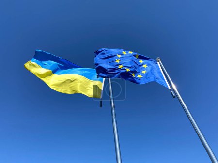 flags of Ukraine and European Union on flagstaffs against blue sky