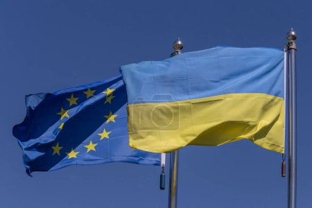 Téléchargez les photos : Drapeaux de l'Ukraine et de l'Union européenne agités sur des mâts de drapeau contre le ciel bleu - en image libre de droit