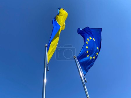 Téléchargez les photos : Drapeaux ukrainiens et de l'Union européenne agités sur des mâts contre le ciel bleu - en image libre de droit