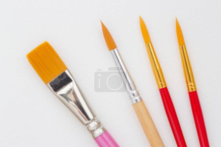Photo for Close up of four paint brushes laying on white paper - Royalty Free Image