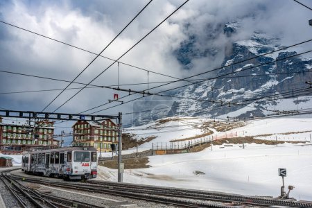 15.04.2022 - kleine scheidegg, schweiz: An einem sonnigen Wintertag fährt eine Zahnradbahn vom Jungfraujoch nach Kleine Scheidegg am verschneiten Hang mit Eiger und Mönch im Hintergrund, in der Schweiz