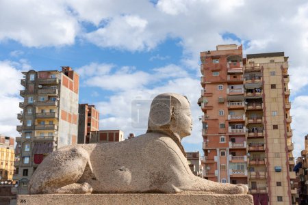 Téléchargez les photos : Sphinx près du pilier de Pompée sur le territoire du Serapeum d'Alexandrie contre des bâtiments résidentiels à plusieurs étages - en image libre de droit