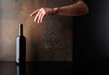 Photo for Hand reaches for a bottle of red wine. A concept image on the theme of expensive wines. Copy space. - Royalty Free Image