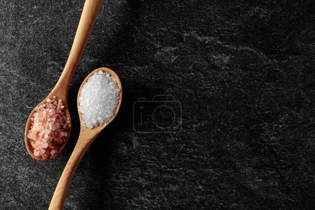Téléchargez les photos : Pink and sea salt in wooden spoons on a black stone background. Copy space. - en image libre de droit