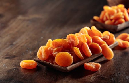 Téléchargez les photos : Abricots secs dans un plat en bois sur une vieille table en bois. - en image libre de droit