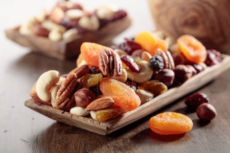 Téléchargez les photos : Mélange de noix et de fruits secs sur une vieille table en bois. Abricots, raisins secs, noix, noisettes, noix de cajou, pacanes et amandes présentés. - en image libre de droit
