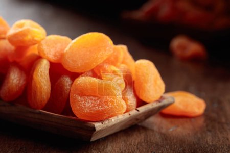 Téléchargez les photos : Abricots secs dans un plat en bois sur une vieille table en bois. - en image libre de droit
