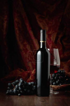 Foto de Bodegón con vino tinto y uvas azules sobre una vieja mesa de madera. - Imagen libre de derechos