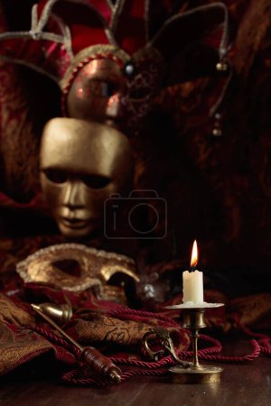 Téléchargez les photos : Bougie allumée dans un vieux chandelier en laiton et masques de carnaval sur une vieille table en bois. - en image libre de droit