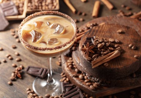 Photo for Irish cream and coffee cocktail in a glass with ice on an old wooden background. Coffee beans, cinnamon, anise, and pieces of chocolate are scattered on the table. - Royalty Free Image