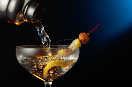 Téléchargez les photos : Martini aux olives vertes et au citron. Le cocktail est versé d'un shaker dans un verre. - en image libre de droit