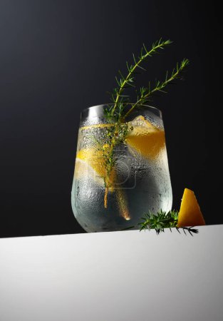 Téléchargez les photos : Cocktail gin tonique avec citron, branche de genièvre et glace sur fond sombre. Espace de copie. - en image libre de droit