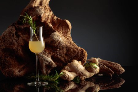 Photo for Ginger liquor with a rosemary branch on a black background with an old snag. - Royalty Free Image