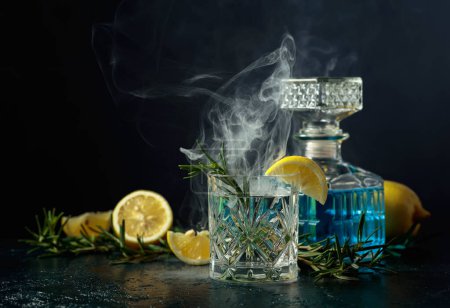 Photo for Cocktail Gin-tonic with lemon and rosemary in a crystal glass. Smoked rosemary old-fashioned cocktail on a table. - Royalty Free Image