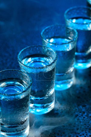 Photo for Wet glasses of vodka in smoke on dark blue background. Selective focus. - Royalty Free Image