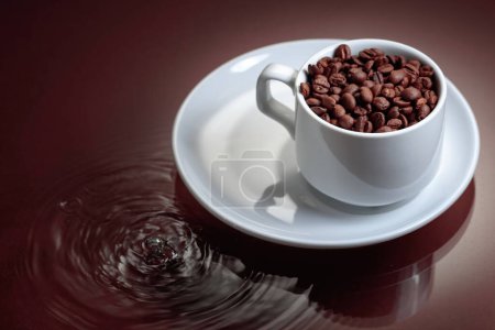 Foto de White cup with coffee beans on a brown background with water ripples. Coffee concept. Copy space. - Imagen libre de derechos