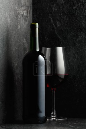 Photo for Bottle and glass of red wine on a black stone background. - Royalty Free Image