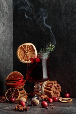 Foto de Bebida caliente de Navidad con especias, cítricos secos y arándanos. Rama de abeto ardiente en un vaso. - Imagen libre de derechos