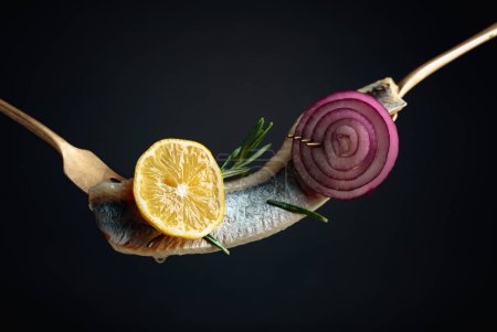 Téléchargez les photos : Filet de hareng à l'huile avec citron, oignon rouge et romarin sur fond noir. - en image libre de droit