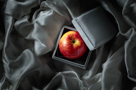 Téléchargez les photos : Une pomme dans une boîte cadeau grise. L'image conceptuelle sur le thème des cadeaux chers. - en image libre de droit