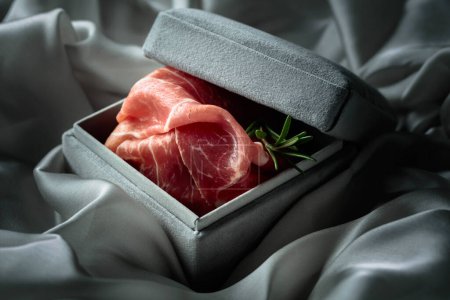Prosciutto con romero en una caja de regalo gris. Concepto del tema de la comida cara.