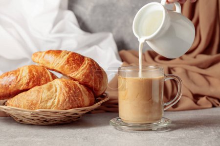 Téléchargez les photos : Freshly baked croissants and coffee with cream. Pouring creme in a glass cup of coffee. - en image libre de droit