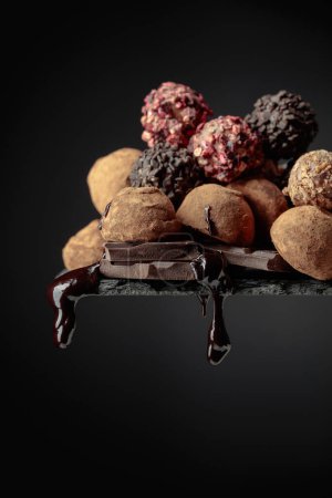 Téléchargez les photos : Délicieuses truffes au chocolat et gouttes de sauce au chocolat sur fond noir. - en image libre de droit
