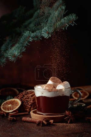 Téléchargez les photos : Chocolat chaud de Noël avec guimauves saupoudrées de cacao en poudre. Photographie de boisson d'hiver sur fond brun foncé. - en image libre de droit