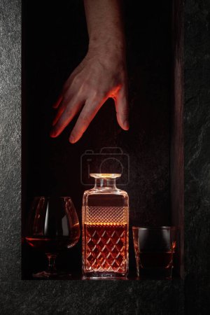 Téléchargez les photos : Main tendue pour une carafe de boisson alcoolisée forte. Une image conceptuelle sur le thème des boissons chères. - en image libre de droit