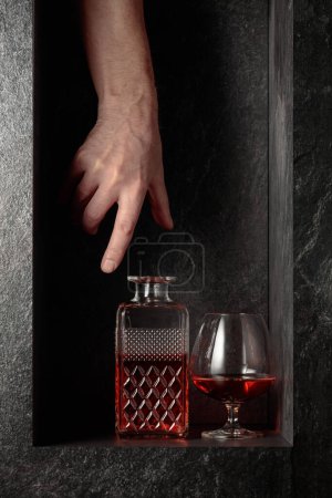 Foto de Alcanzar la mano para un decantador de brandy. Una imagen conceptual sobre el tema de las bebidas caras. - Imagen libre de derechos
