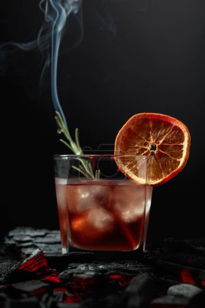 Photo for Old-fashioned cocktail with ice, dried orange slice, and rosemary. Whiskey with rosemary and beautiful swirls of smoke on a black background. - Royalty Free Image