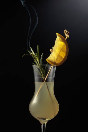 Téléchargez les photos : Limoncello dans un verre. Une liqueur de citron italienne sucrée, une boisson alcoolisée forte traditionnelle garnie d'une branche de romarin fumante. - en image libre de droit