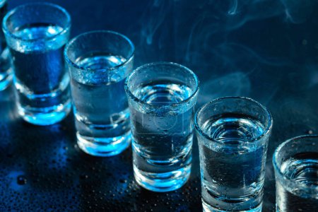 Photo for Wet glasses of vodka in smoke on dark blue background. Selective focus. - Royalty Free Image