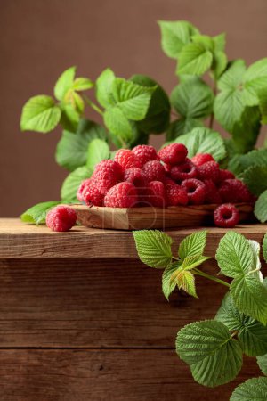 Photo for Ripe juicy raspberries with leaves. Berries in a wooden dish on an old wooden table. - Royalty Free Image