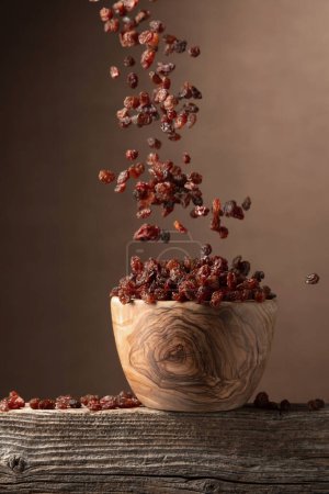Téléchargez les photos : Voler raisins secs sur un fond brun. Raisins dans un bol en bois. Espace de copie. - en image libre de droit