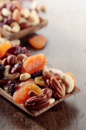 Téléchargez les photos : Mélange de noix et de fruits secs sur une vieille table en bois. Abricots, raisins secs, noix, noisettes, noix de cajou, pacanes et amandes présentés. - en image libre de droit