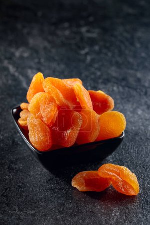 Téléchargez les photos : Abricots secs dans un petit plat en céramique sur une table en pierre noire. - en image libre de droit
