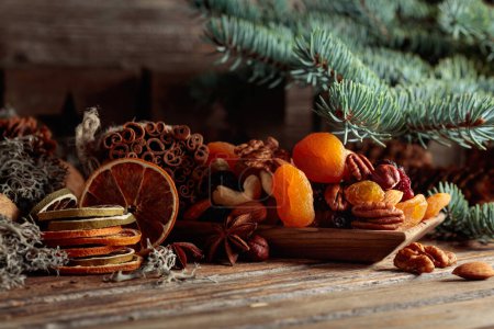 Foto de Frutas secas y frutos secos sobre una vieja mesa de madera. Bodegón de Navidad con cítricos secos, albaricoques, pasas, varias nueces, palitos de canela y anís. - Imagen libre de derechos