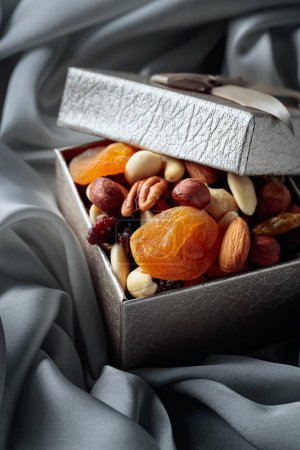 Téléchargez les photos : Fruits secs et noix dans un coffret cadeau sur un chiffon gris. - en image libre de droit