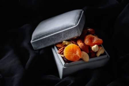 Téléchargez les photos : Fruits secs et noix dans une boîte cadeau sur un chiffon noir. - en image libre de droit