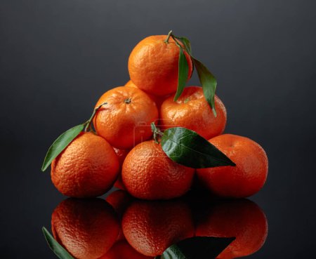 Foto de Mandarinas o clementinas con hojas verdes sobre fondo negro reflectante. - Imagen libre de derechos