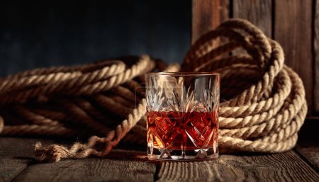 Photo for Crystal glass with rum, cognac, or whiskey on an old wooden background. - Royalty Free Image