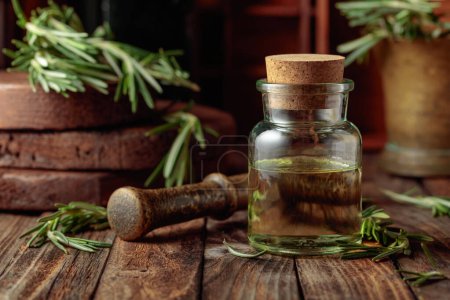 Photo for Rosemary essential oil or infusion on an old wooden table. Aromatherapy, spa, and herbal medicine ingredients. - Royalty Free Image