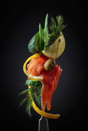 Foto de Rebanadas de salmón en un tenedor. Salmón ahumado con eneldo, pepino, alcaparras, cebolla verde y rodaja de limón. - Imagen libre de derechos