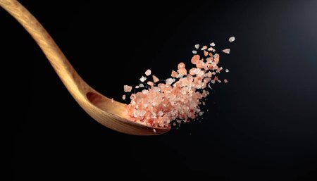 Photo for Pink Himalayan salt is poured with a wooden spoon. Himalaya salt on a dark background. Copy space. - Royalty Free Image