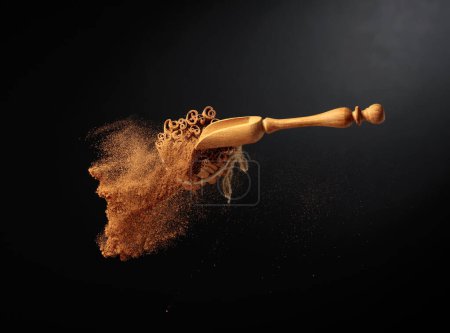 Photo for Cinnamon powder is poured out of the wooden spoon. The ground cinnamon and cinnamon sticks, tied with jute rope on a black background. - Royalty Free Image