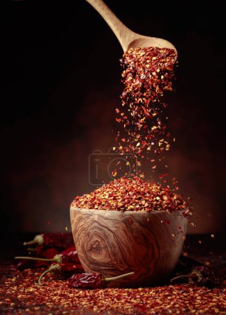 Photo for Chilli flakes are poured into a wooden dish. Chilli flakes and dried chili peppers on a brown background. - Royalty Free Image