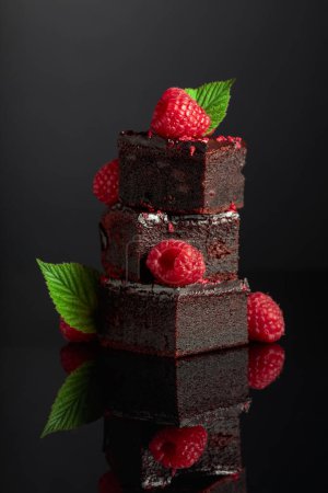 Photo for Chocolate cake garnished with fresh raspberries on a black reflective background. - Royalty Free Image