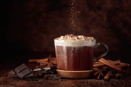 Foto de Chocolate caliente con crema batida espolvoreada con migas de chocolate. Chocolate caliente con ingredientes en una mesa marrón. - Imagen libre de derechos